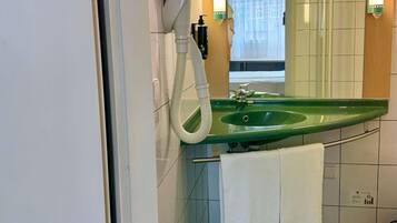A bathroom with a green sink, a hairdryer, a mirror, and a towel hanging on the wall.