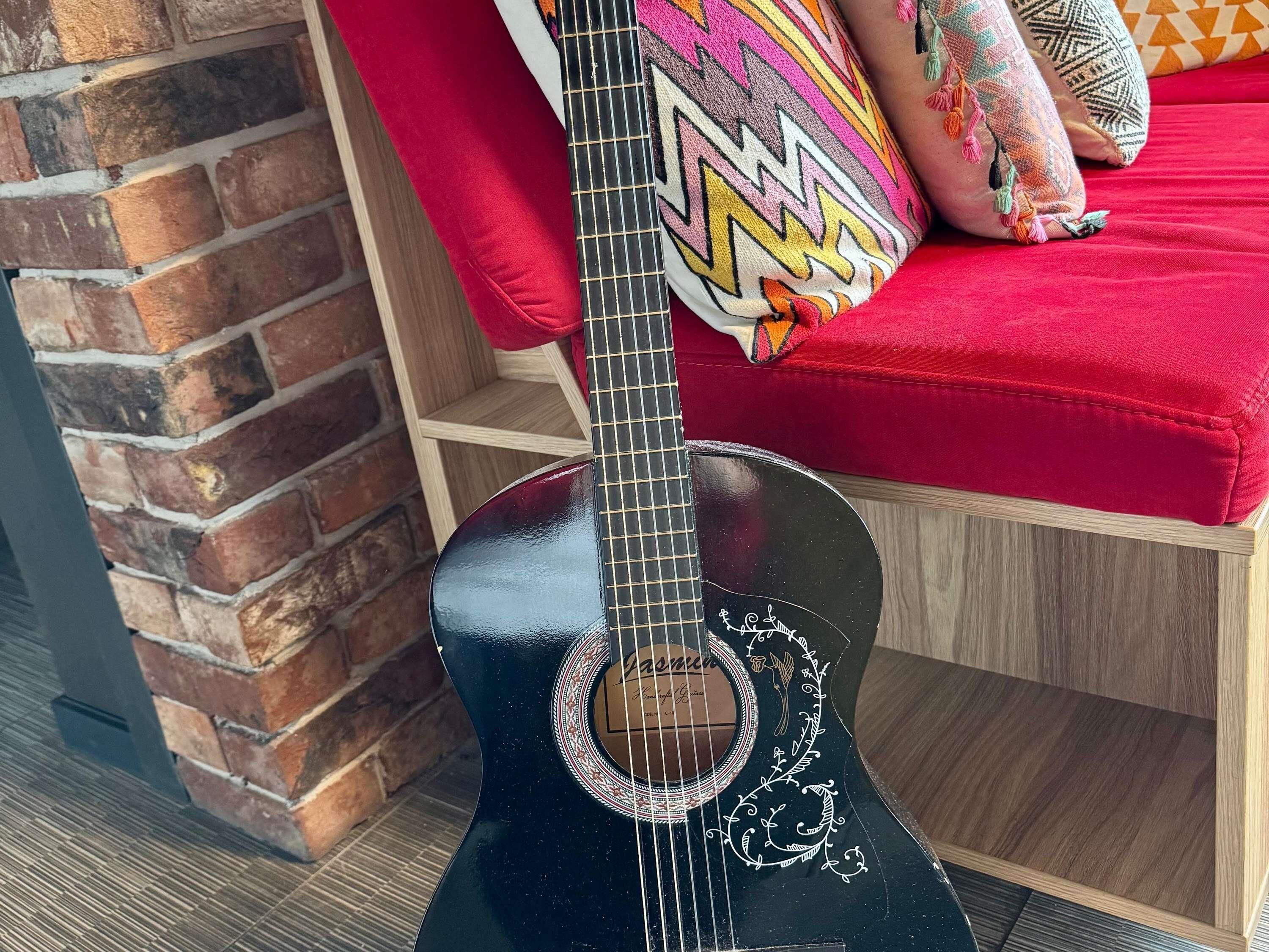 A black guitar with decorative patterns, a brick wall, and a red cushioned bench with patterned pillows.