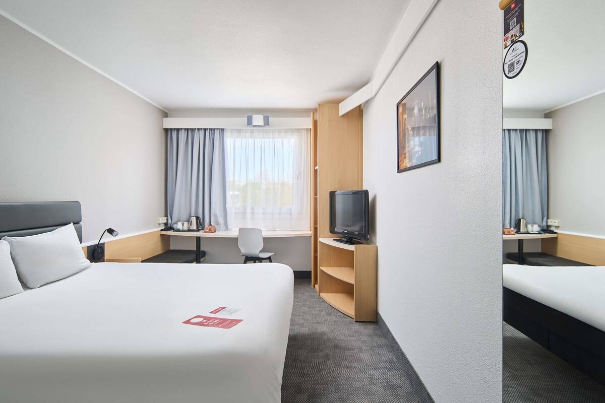 Una habitación de hotel con una cama, un escritorio, un televisor y una pequeña zona de estar.