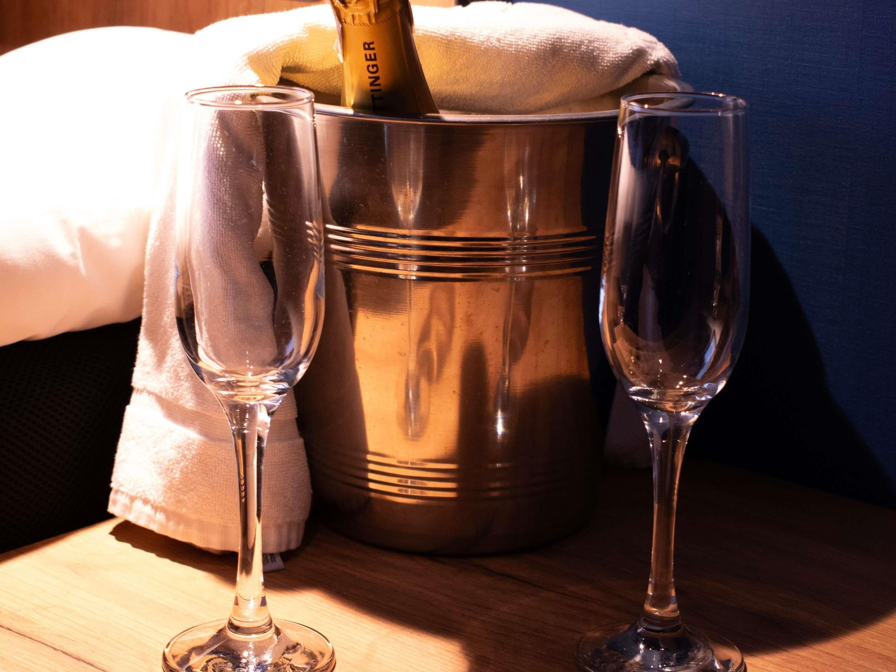 Twee lege wijnglazen, een metalen emmer en een fles champagne.