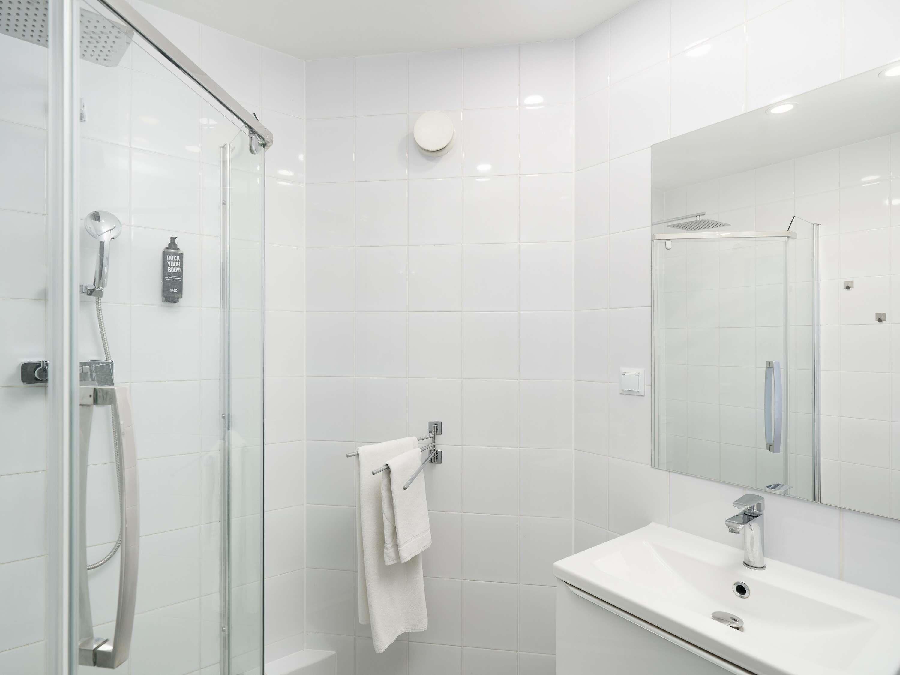 A modern bathroom with a glass shower enclosure, a white sink, and a large mirror.