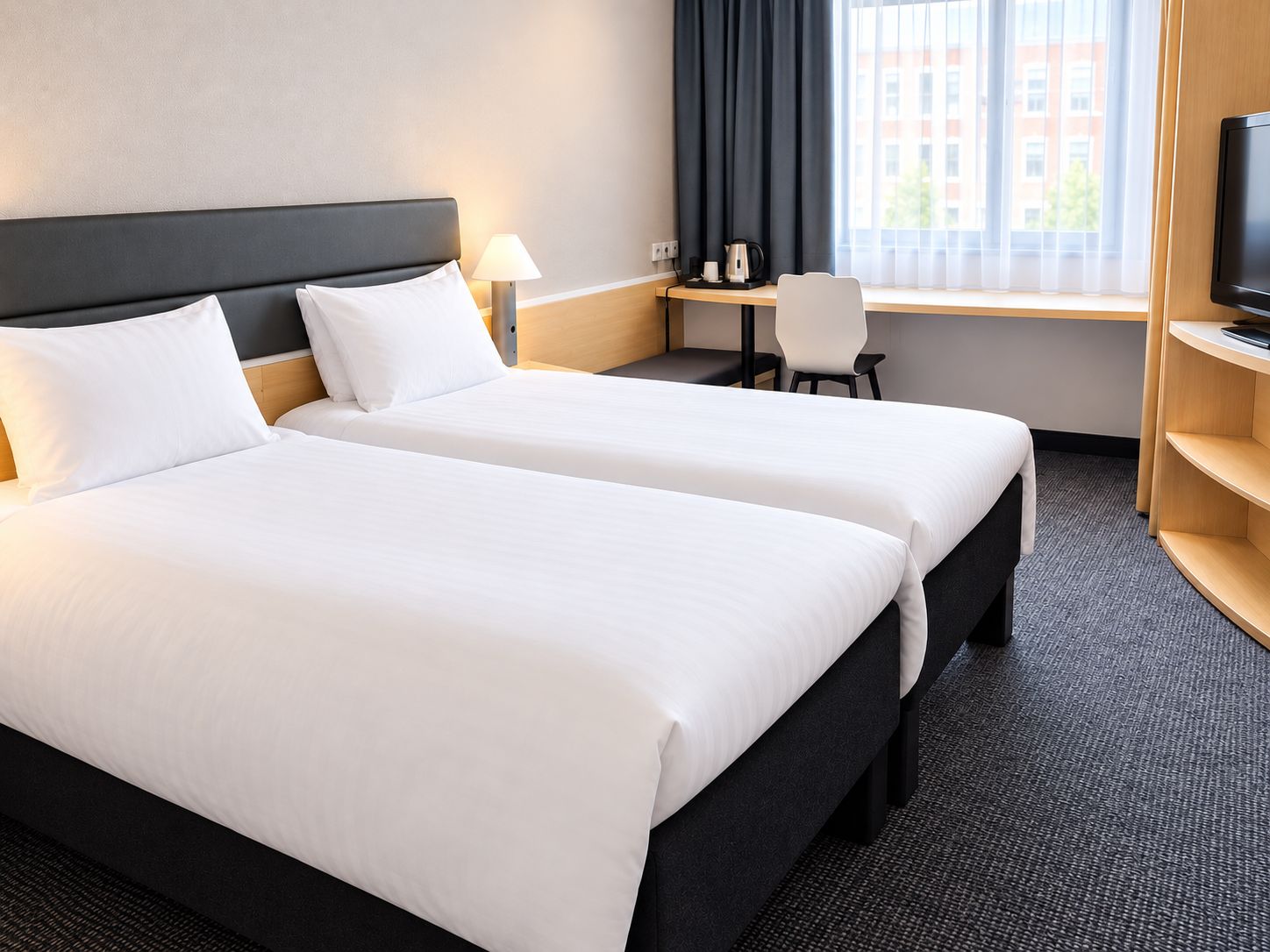 Habitación de hotel con dos camas, un escritorio, una silla, un televisor y una ventana con cortinas.