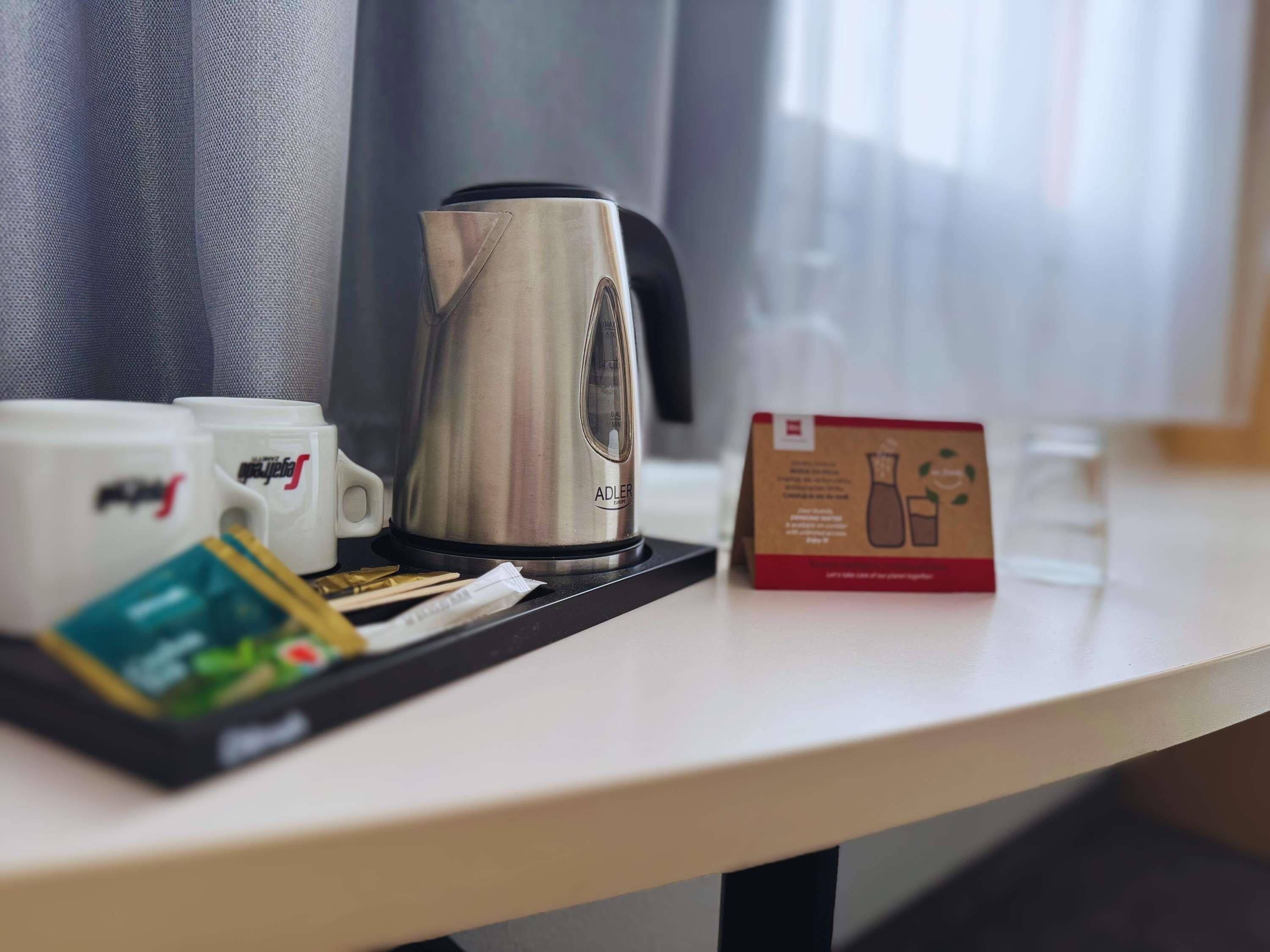 Habitación de hotel con cafetera, tazas, bandeja con bolsitas de té y un cartel sobre la mesa.