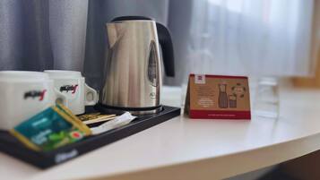 Habitación de hotel con cafetera, tazas, bandeja con bolsitas de té y un cartel sobre la mesa.