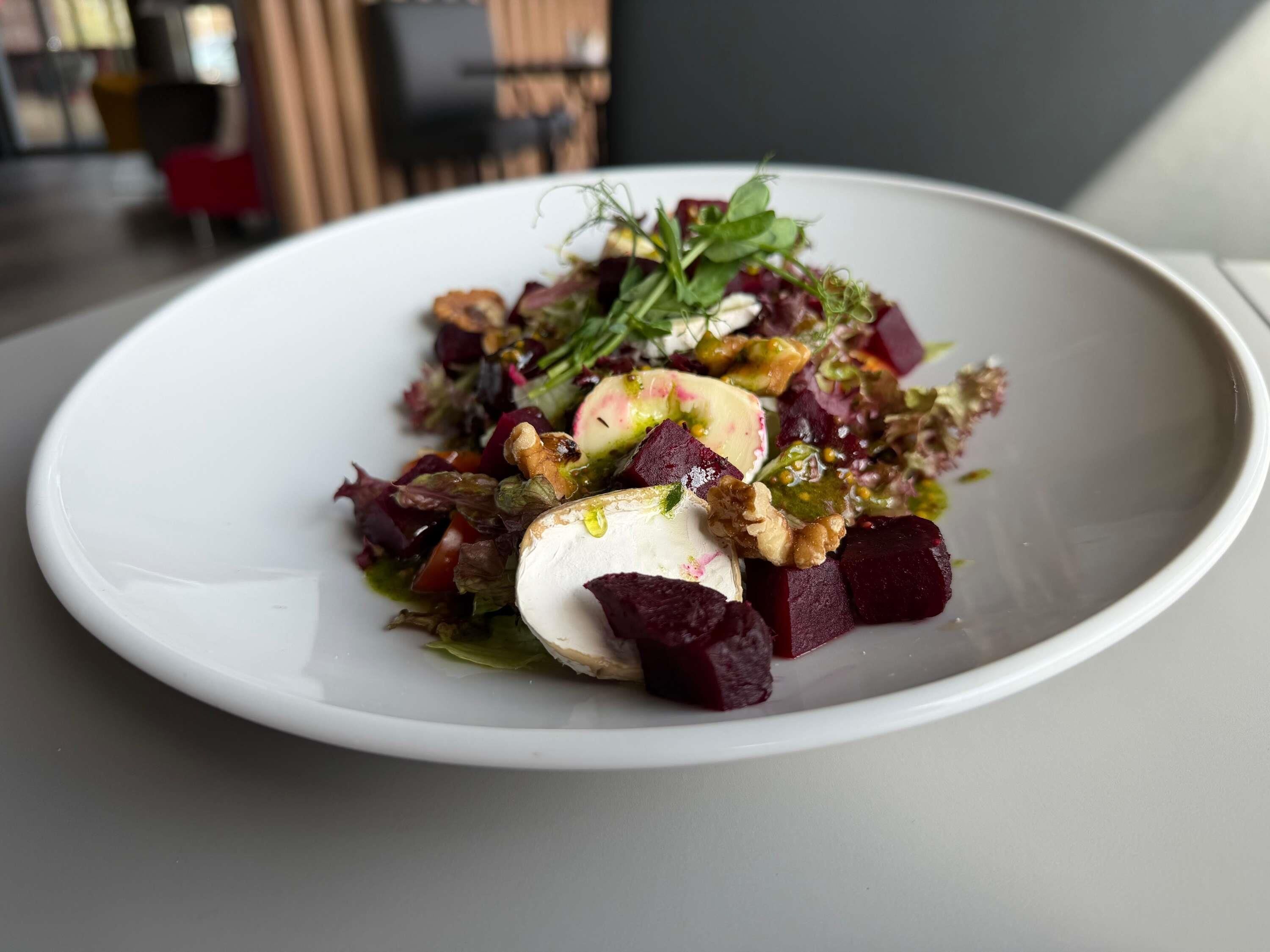 A white plate with a salad containing beets, nuts, and greens.
