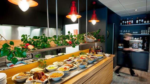 Ein reichhaltiges Buffet mit verschiedenen Speisen, eine Bar mit Flaschen und ein Barista, der Getränke zubereitet.