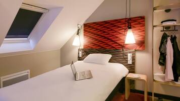 Ein modernes Hotelzimmer mit Oberlicht, einem Bett mit Laptop, einer roten Wand mit Muster und einem Kleiderständer.