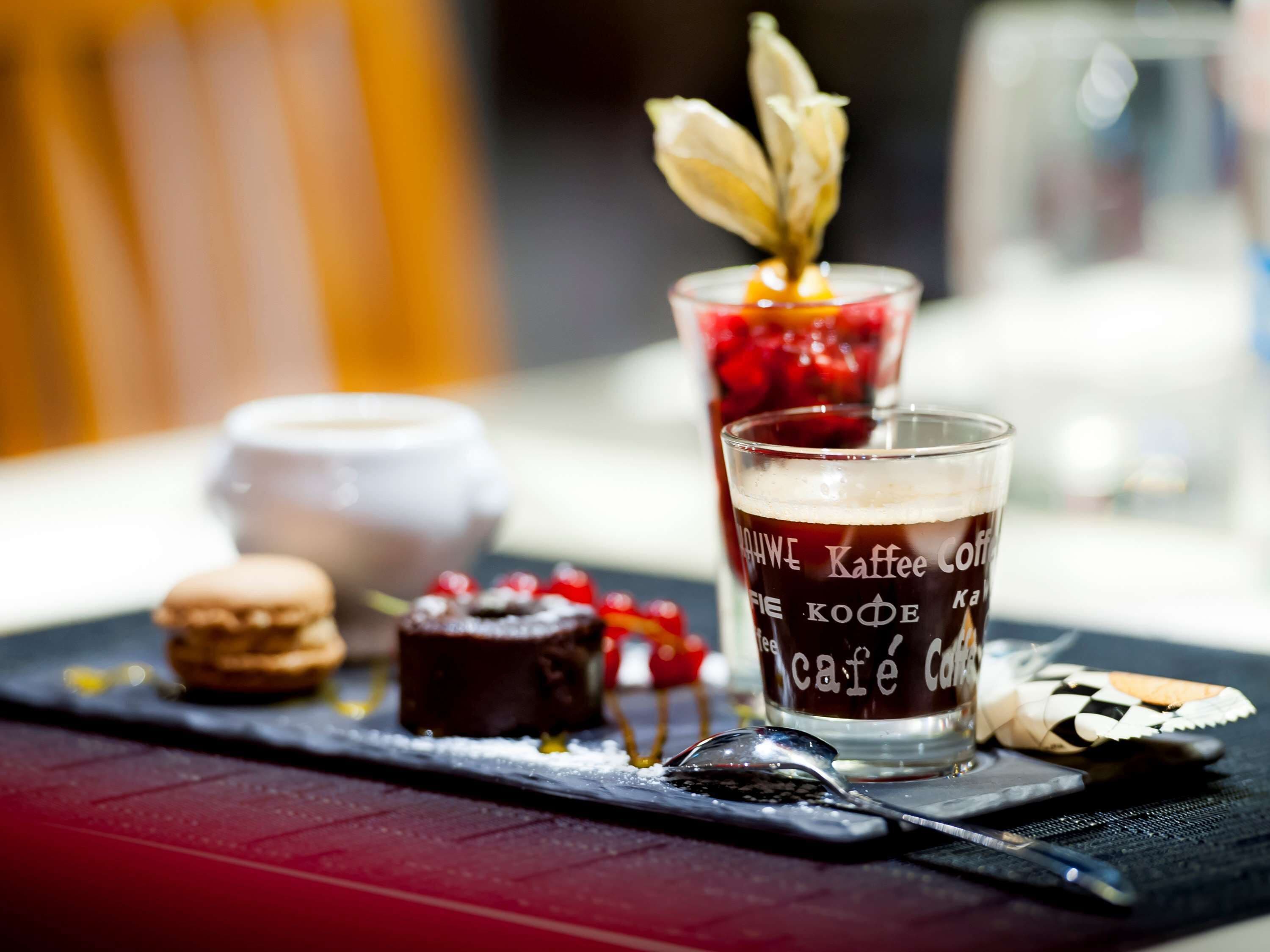 A dessert tray with macarons, a chocolate tart, and a glass of coffee with a decorative flower.