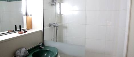 A bathroom with a green sink, a mirror, and a shower area.