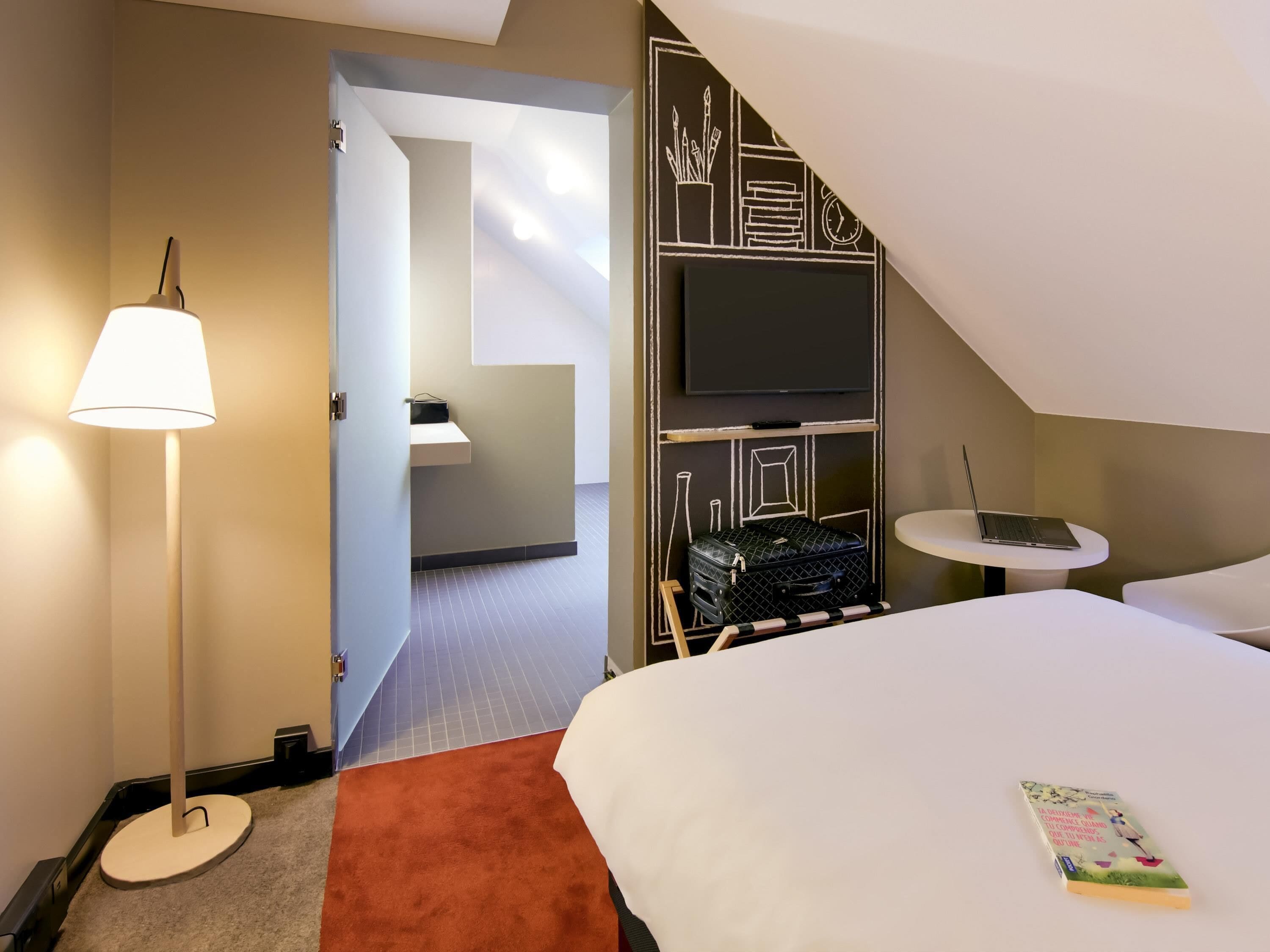 Une chambre d’hôtel avec un lit, un bureau avec un ordinateur portable, une télévision et une bibliothèque.