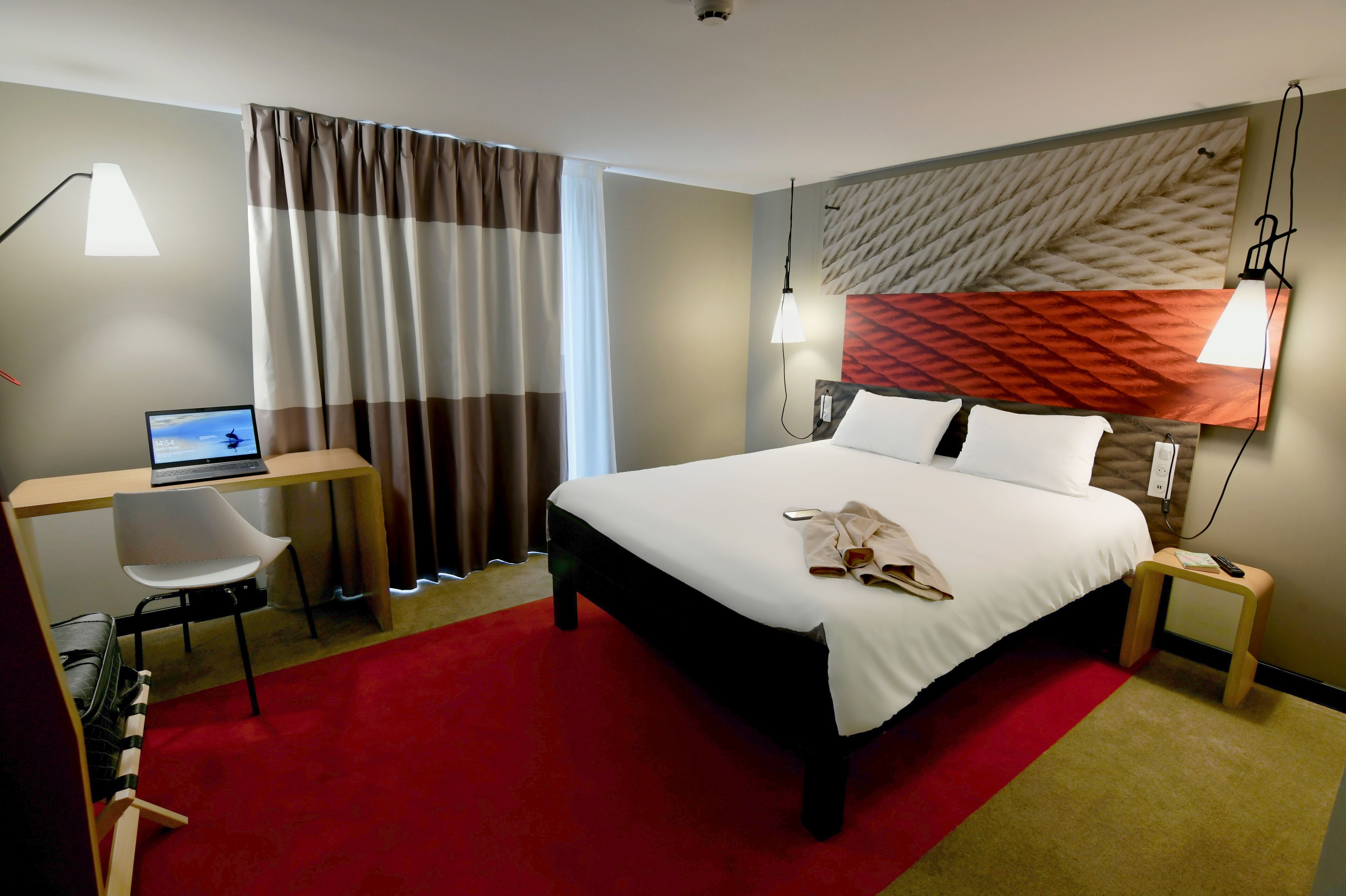 Una habitación de hotel con cama, escritorio, silla y una computadora portátil.