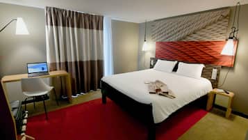 Una habitación de hotel con cama, escritorio, silla y una computadora portátil.
