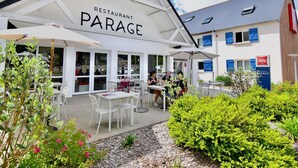 Ein Restaurant namens PARAGE mit Außenbereich, weißen Tischen und Sonnenschirmen.