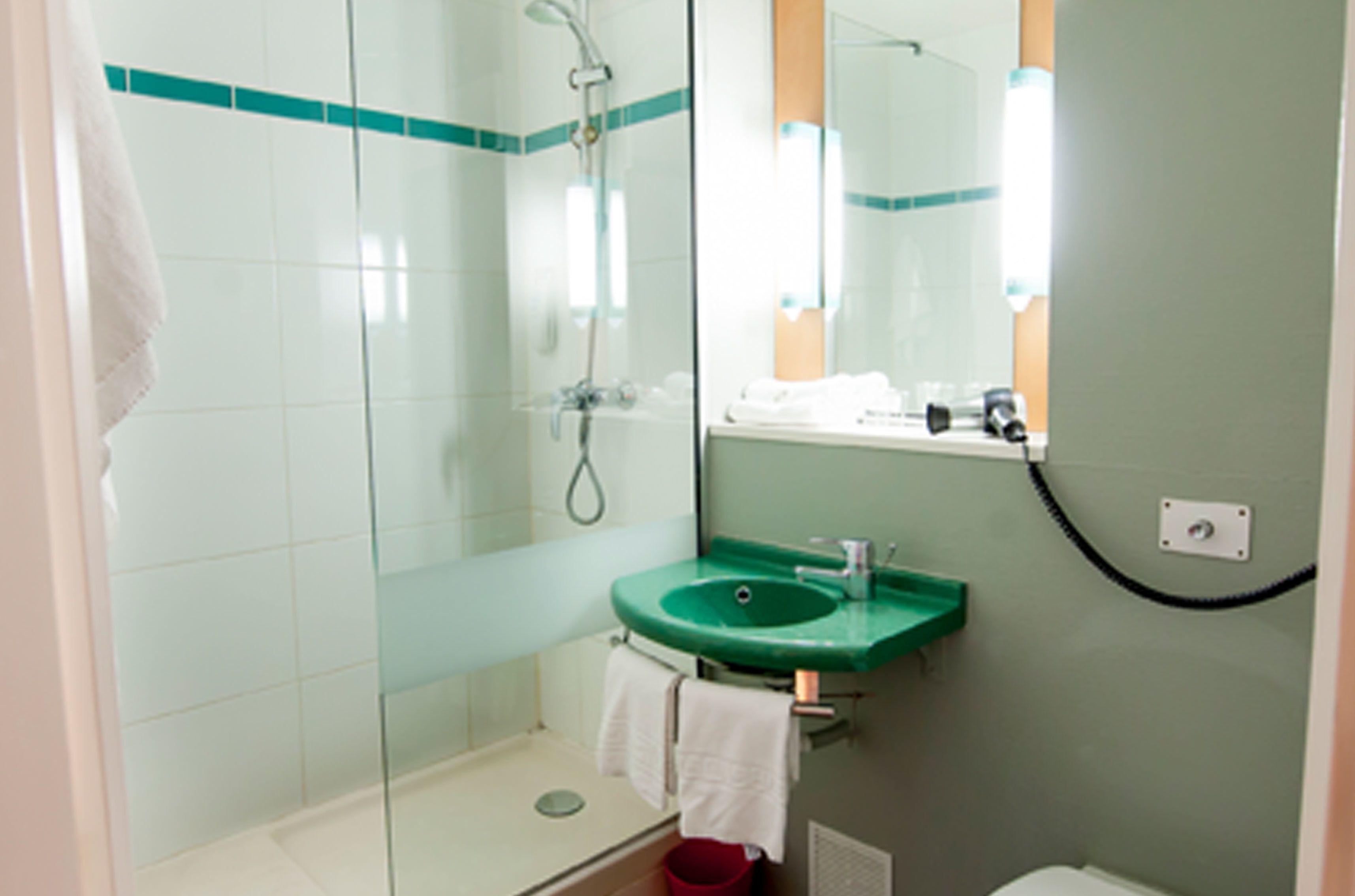 Un baño con ducha de vidrio, un lavamanos verde y un espejo encima.