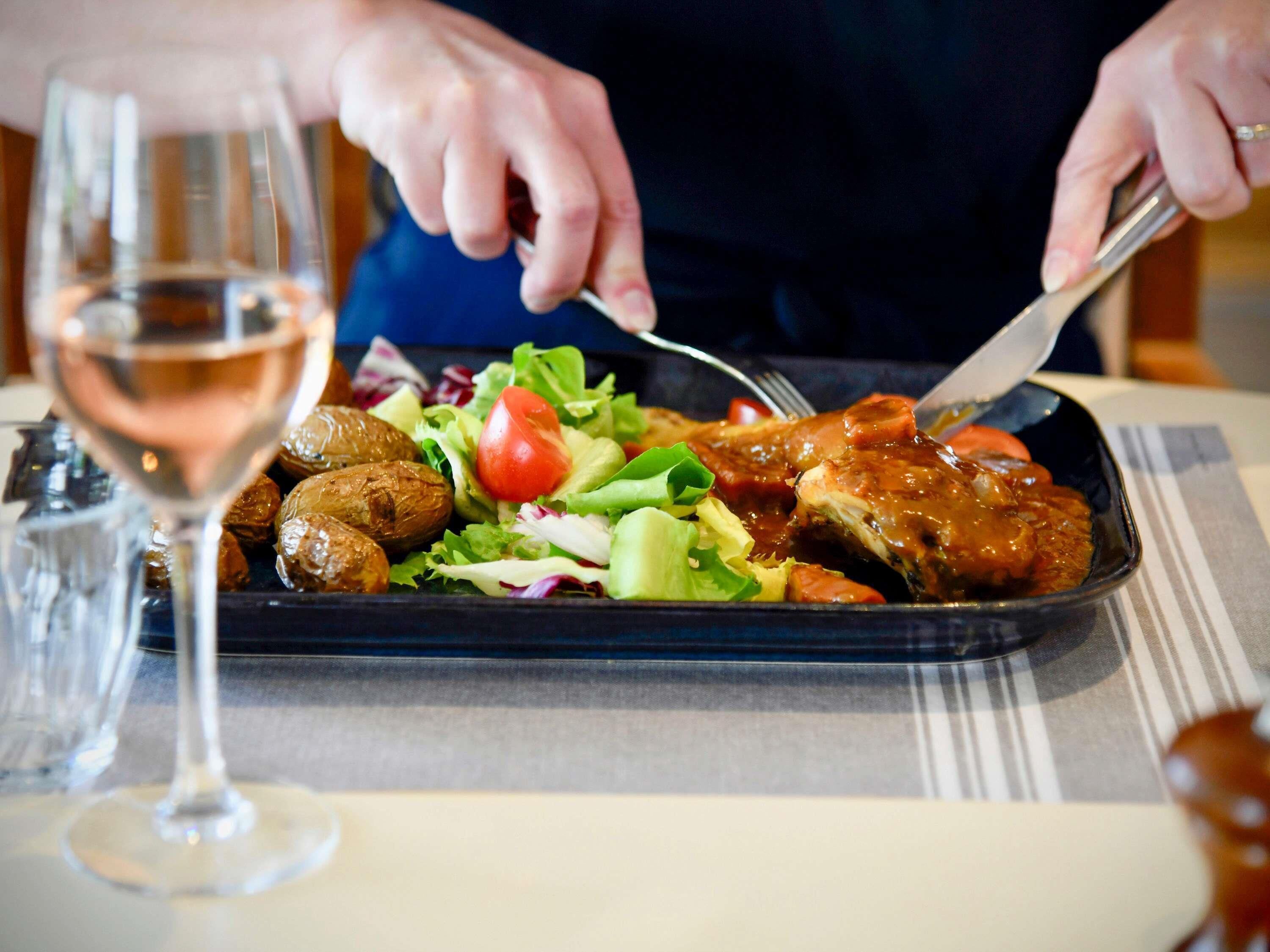 A person dining with a plate of food, a glass of wine, and a fork.