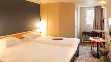 A hotel room with a large bed, a desk, a chair, a small table, and a window with curtains.