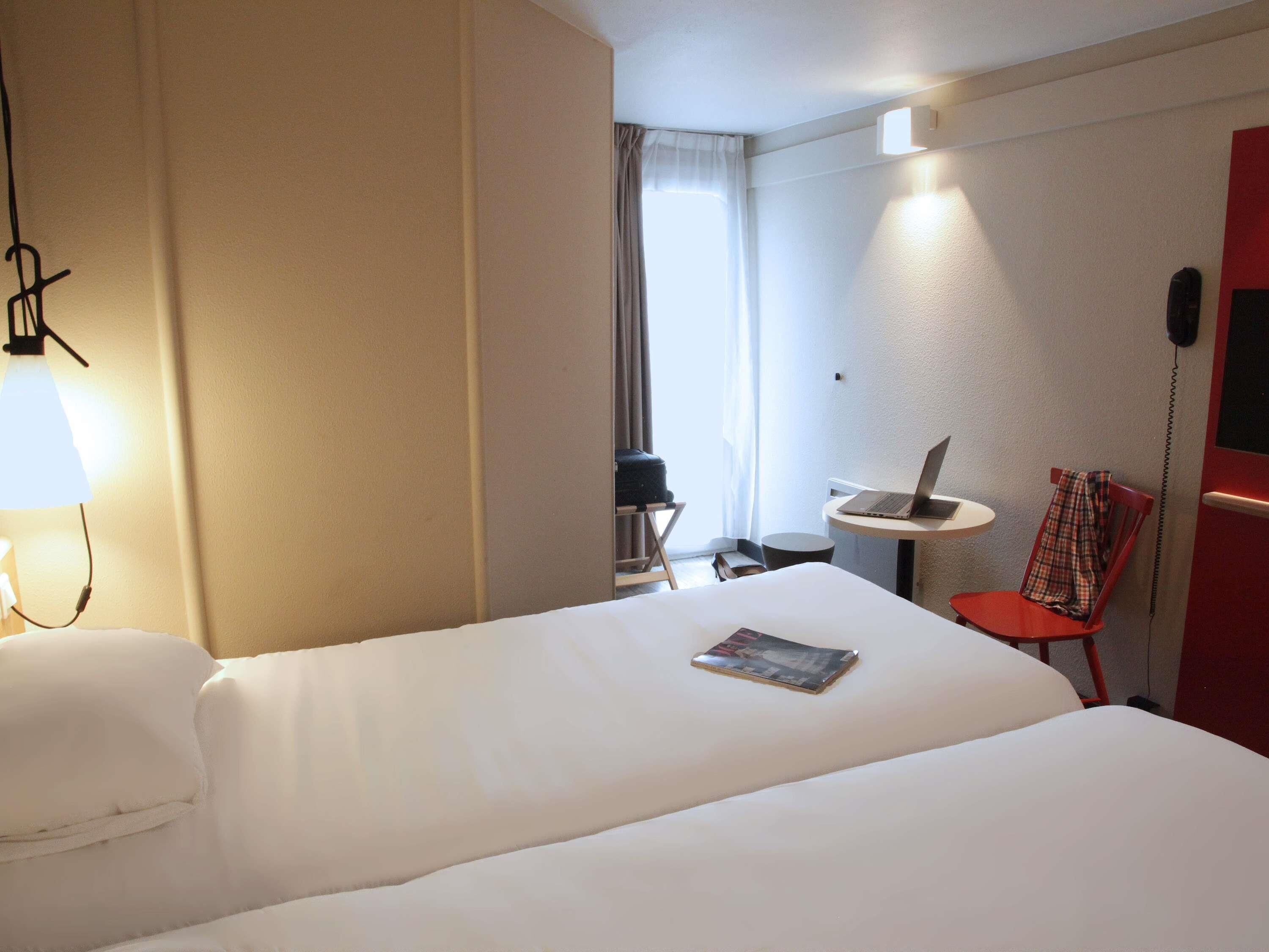 Ett hotellrum med en säng, ett skrivbord, en stol, en lampa och ett fönster.