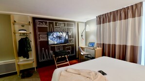 Ein Hotelzimmer mit Bett, Schreibtisch mit Computer, Wandfernseher und Kleiderschrank.