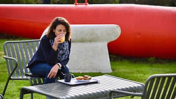 A person sitting on a metal bench outdoors with a tray of food and a drink.