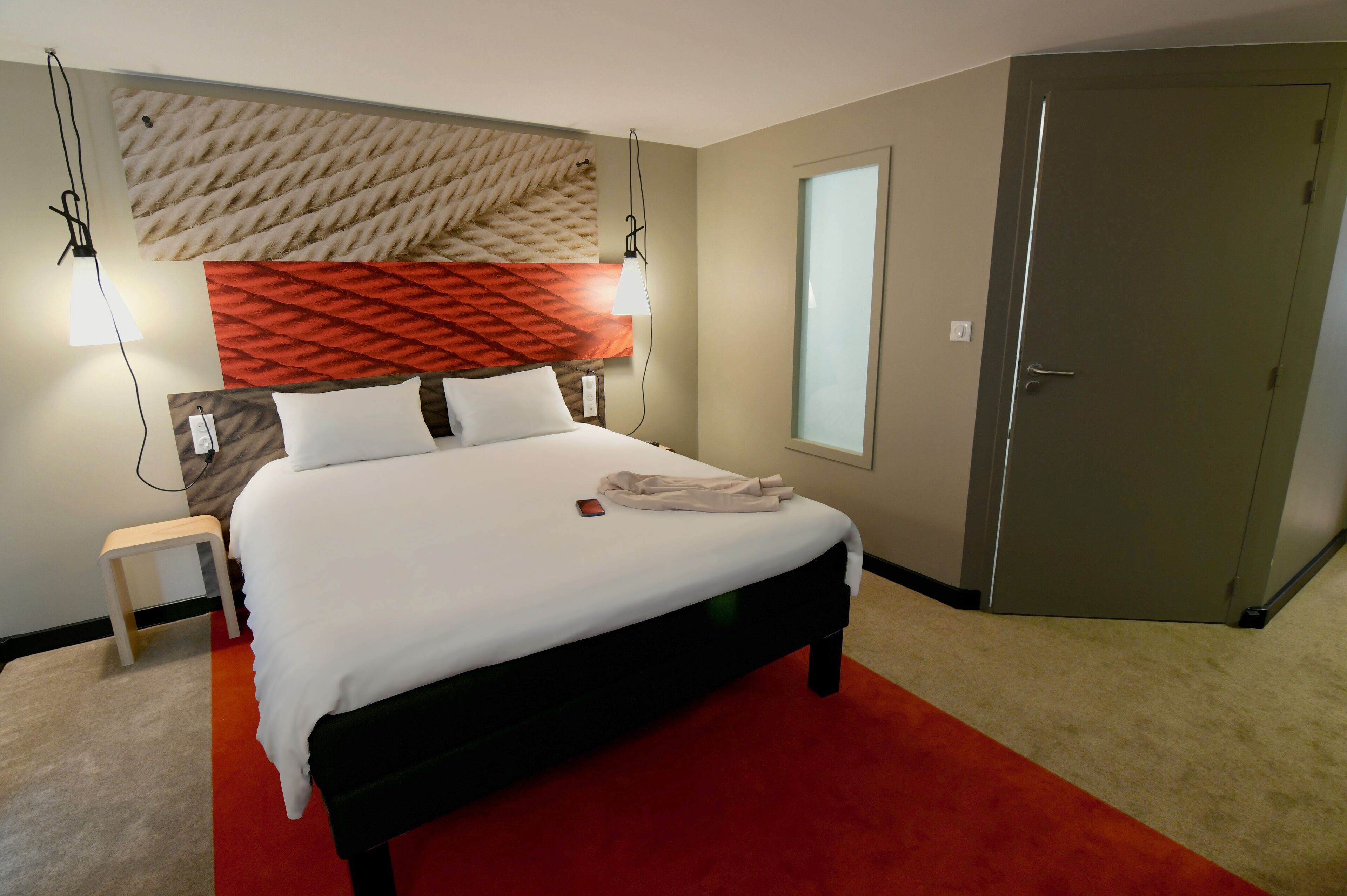 Una habitación de hotel con cama, mesita de noche, lámpara y armario.