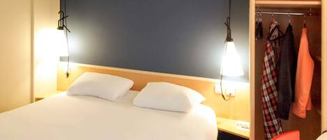 A hotel room with a bed, bedside lamps, a nightstand, a red chair, and a coat rack with clothes.