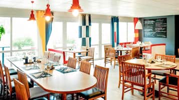 Un restaurant doté de nombreuses tables et chaises, de grandes fenêtres et de luminaires suspendus.