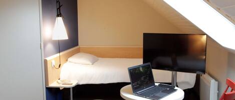 A compact hotel room with a bed, a desk with a laptop, a chair, and a small table.