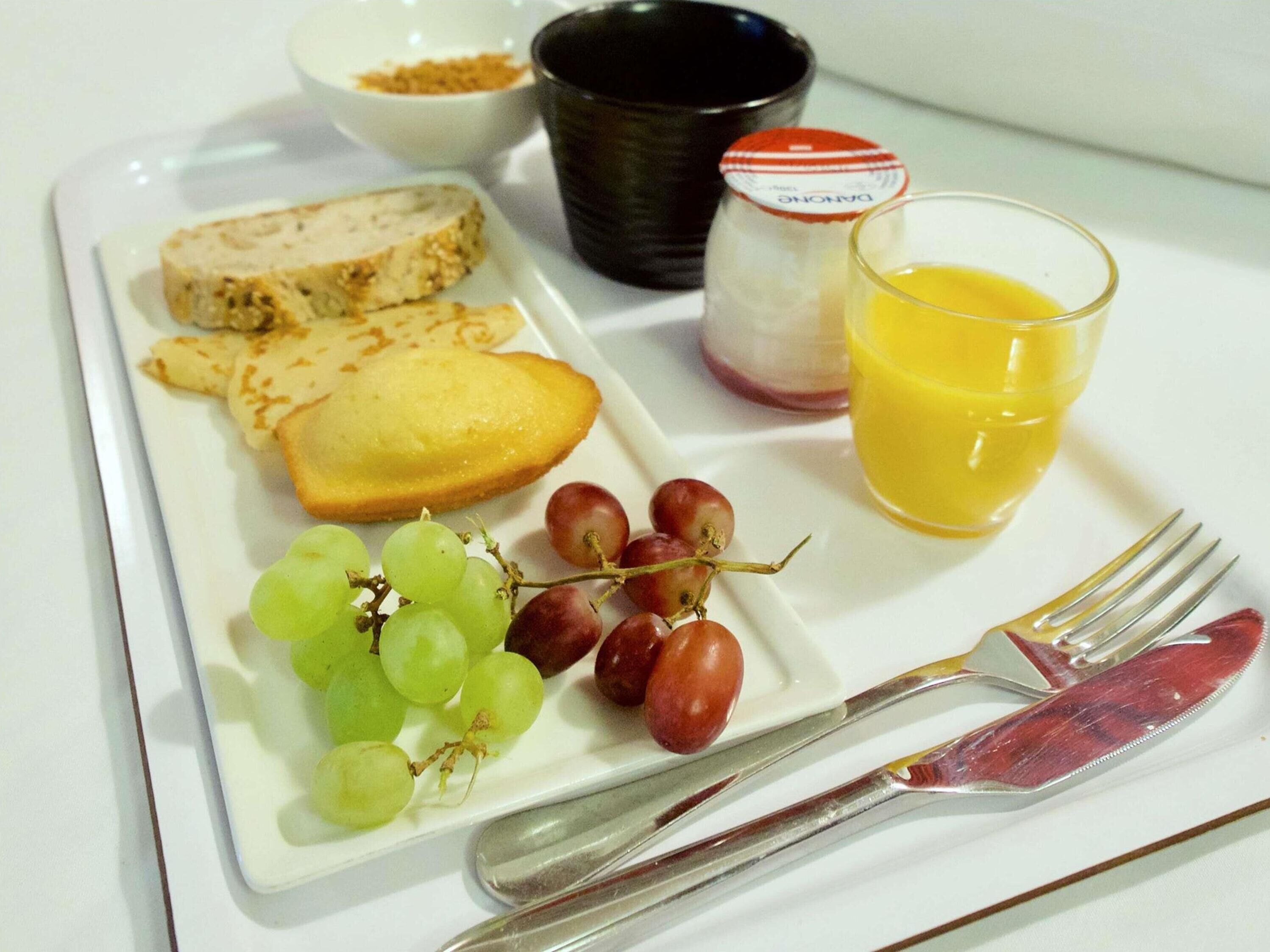Un plato de desayuno con pan, uvas, un vaso de jugo de naranja y un frasco de mermelada.