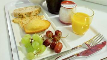 Une assiette de petit-déjeuner avec du pain, des raisins, un verre de jus d’orange et un pot de confiture.
