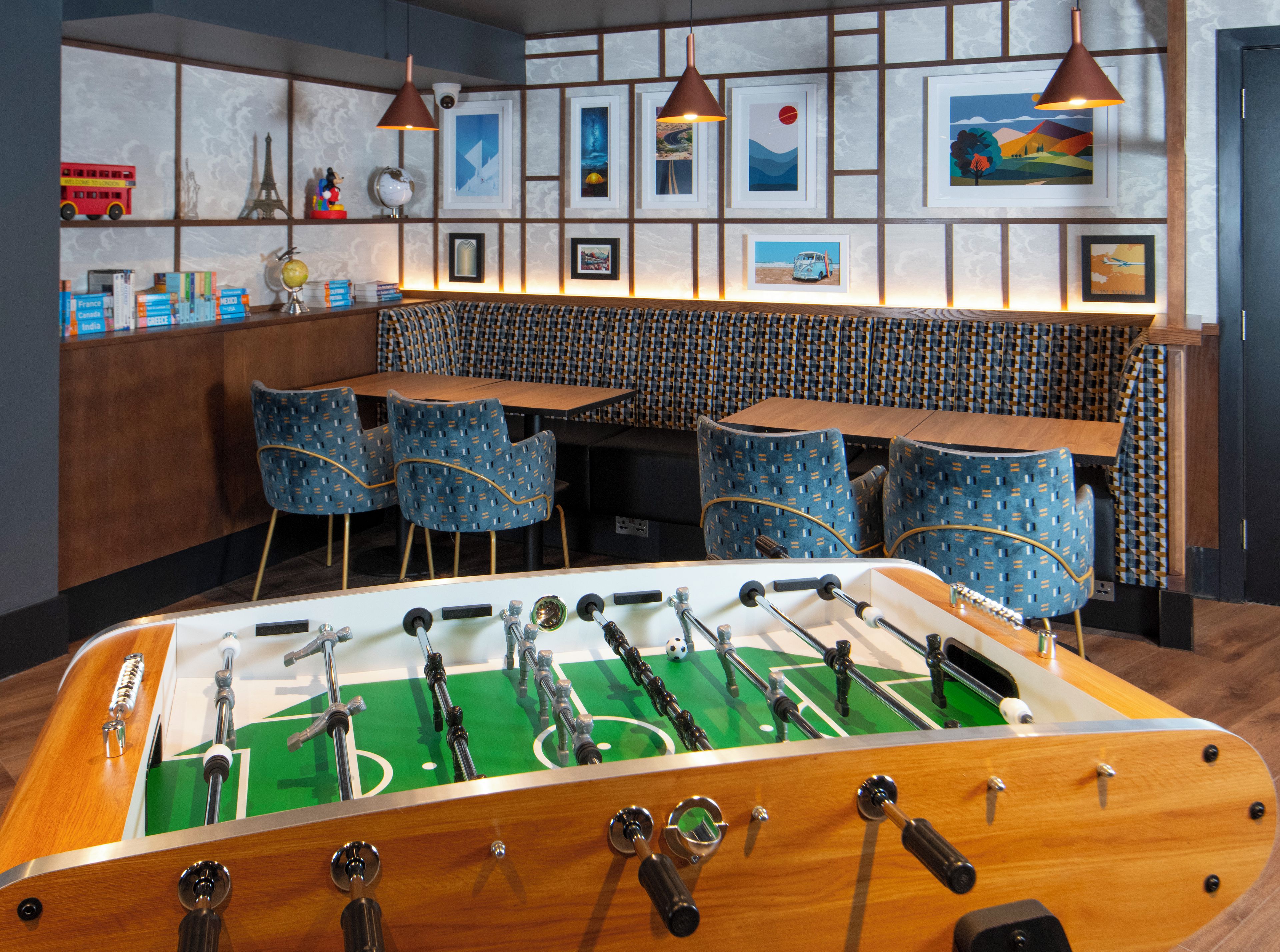 Una habitación con mesa de fútbolín, una zona de bar con sillas y una pared decorada con fotografías enmarcadas.