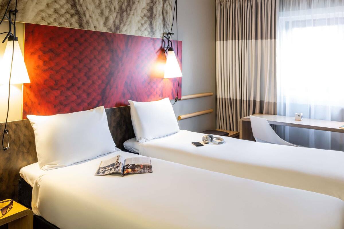 Ein Hotelzimmer mit zwei Betten, einem Schreibtisch und einem großen Fenster mit Vorhängen.