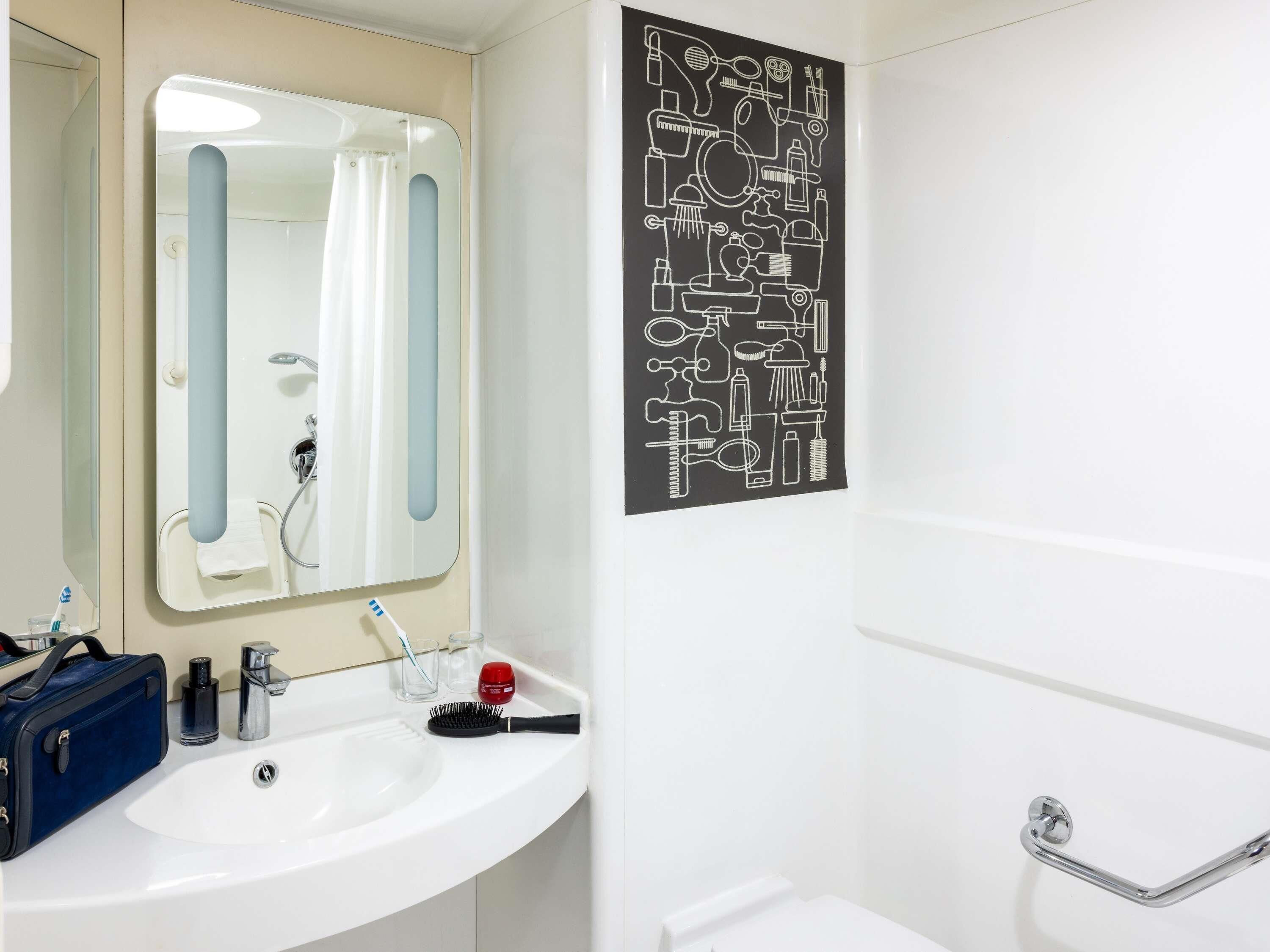 A bathroom with a white sink, mirror, and shower. There is a black and white poster on the wall.