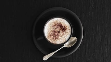 A cup of coffee with a spoon on a black saucer.