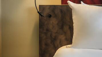 A neatly made bed with white linens, a wooden nightstand with a lamp, and a red textured wall behind the bed.