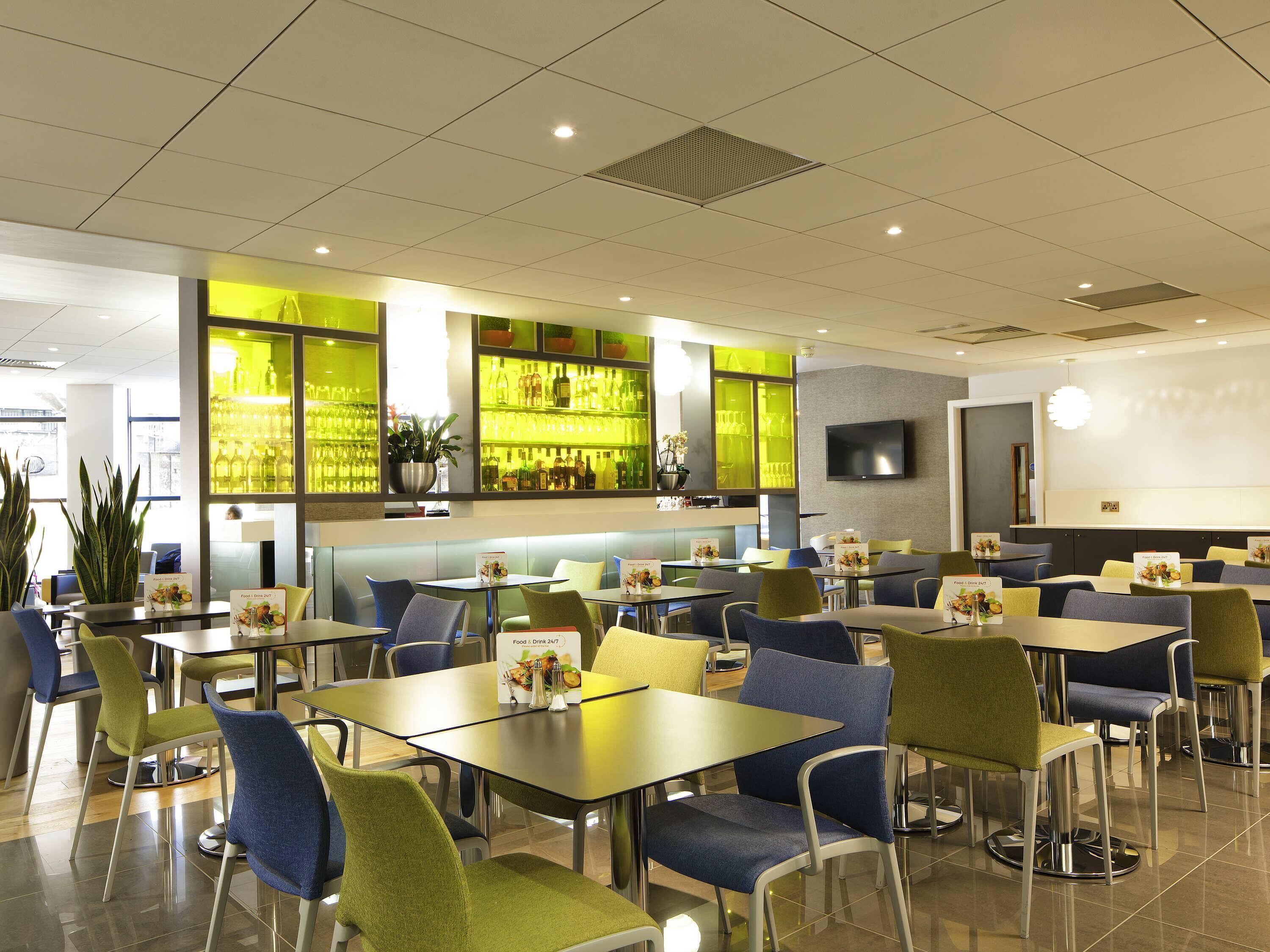 Um restaurante moderno com cabines e mesas, área de bar com garrafas e uma TV de tela plana na parede.