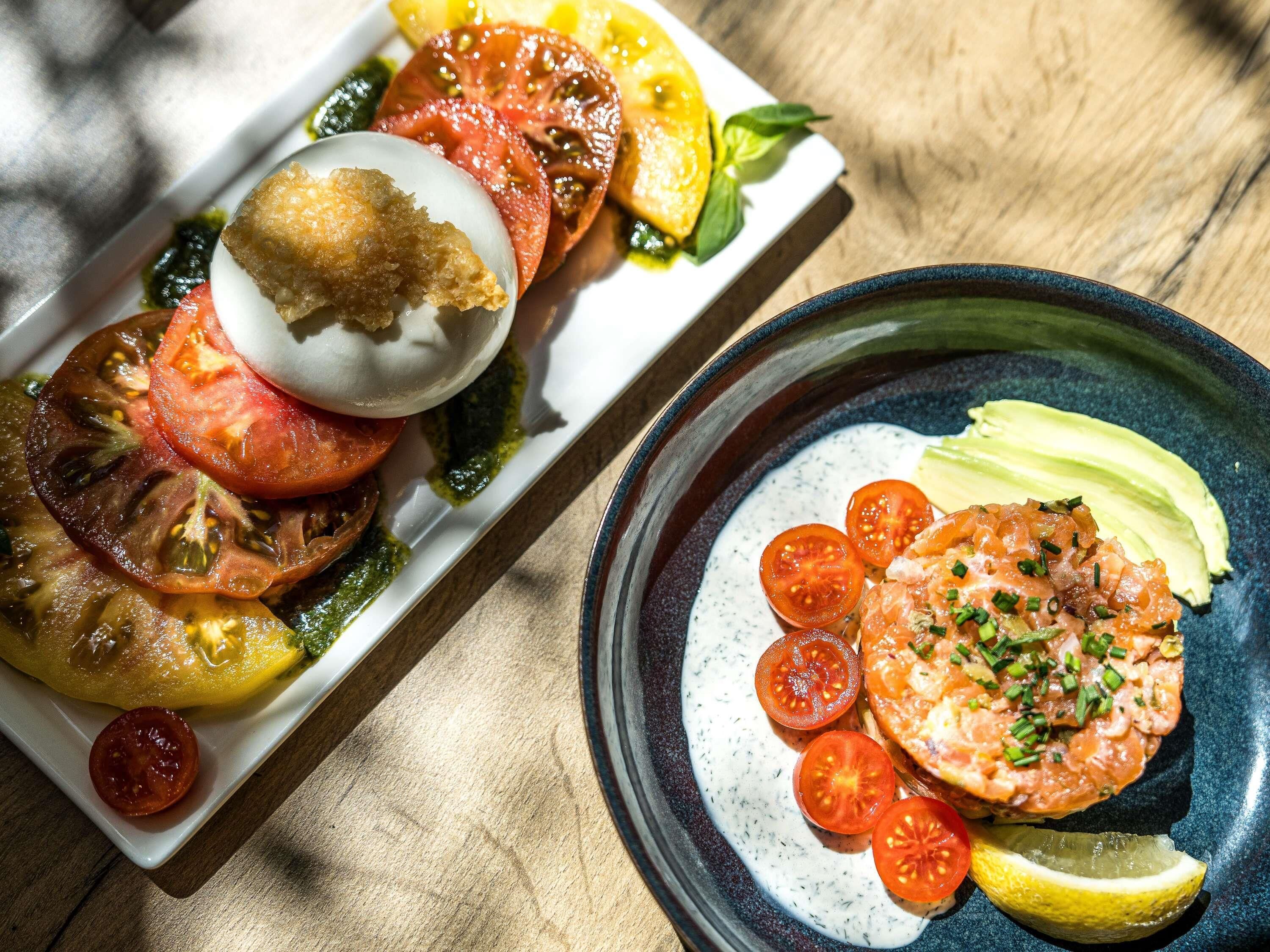 Un plato de comida con tomates, aguacate y una rodaja de limón.