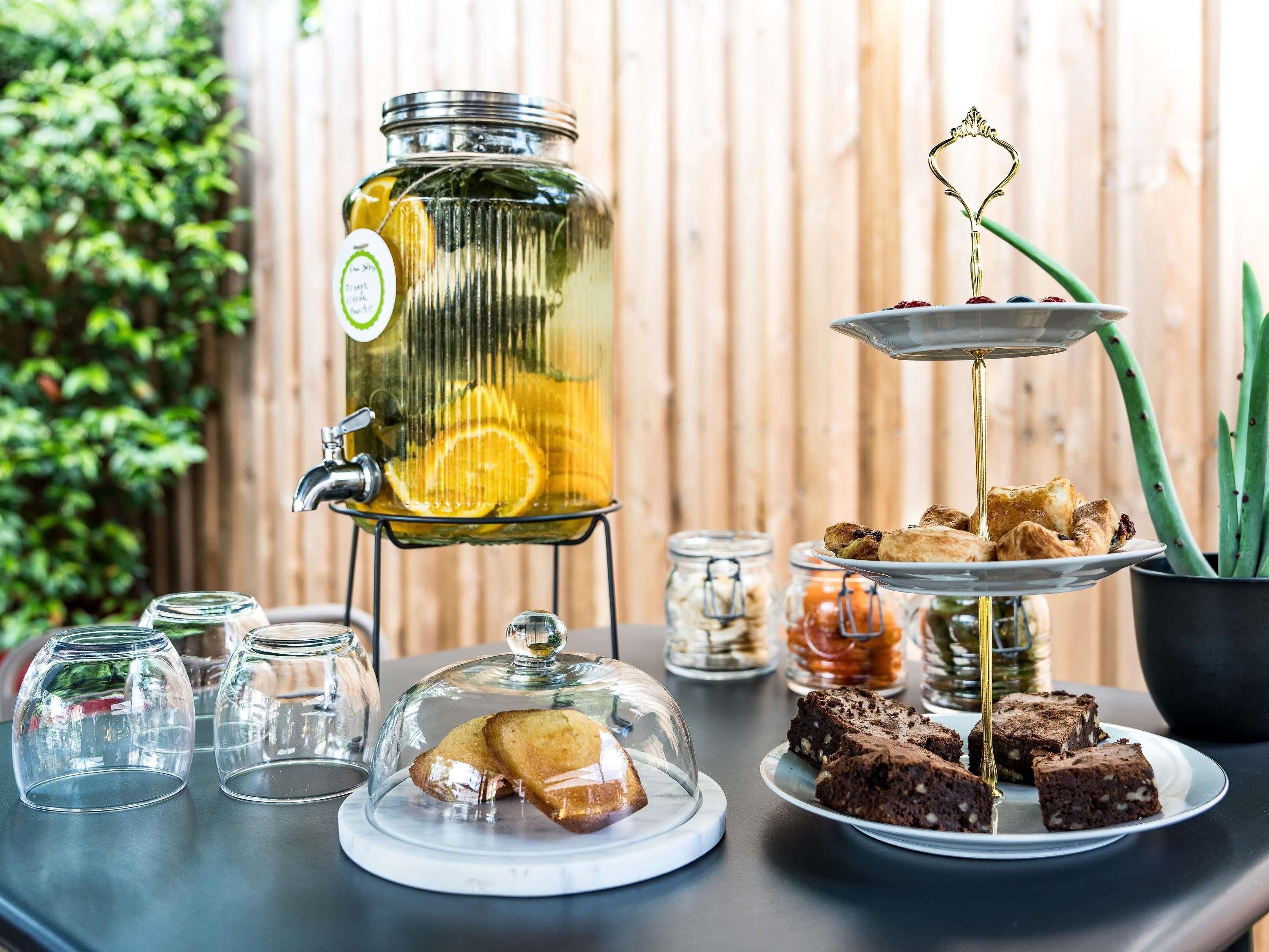 Un dispensador de bebidas con tapa de vidrio, un expositor escalonado para postres con brownies, y una claraboya de cristal sobre una bandeja de pasteles.
