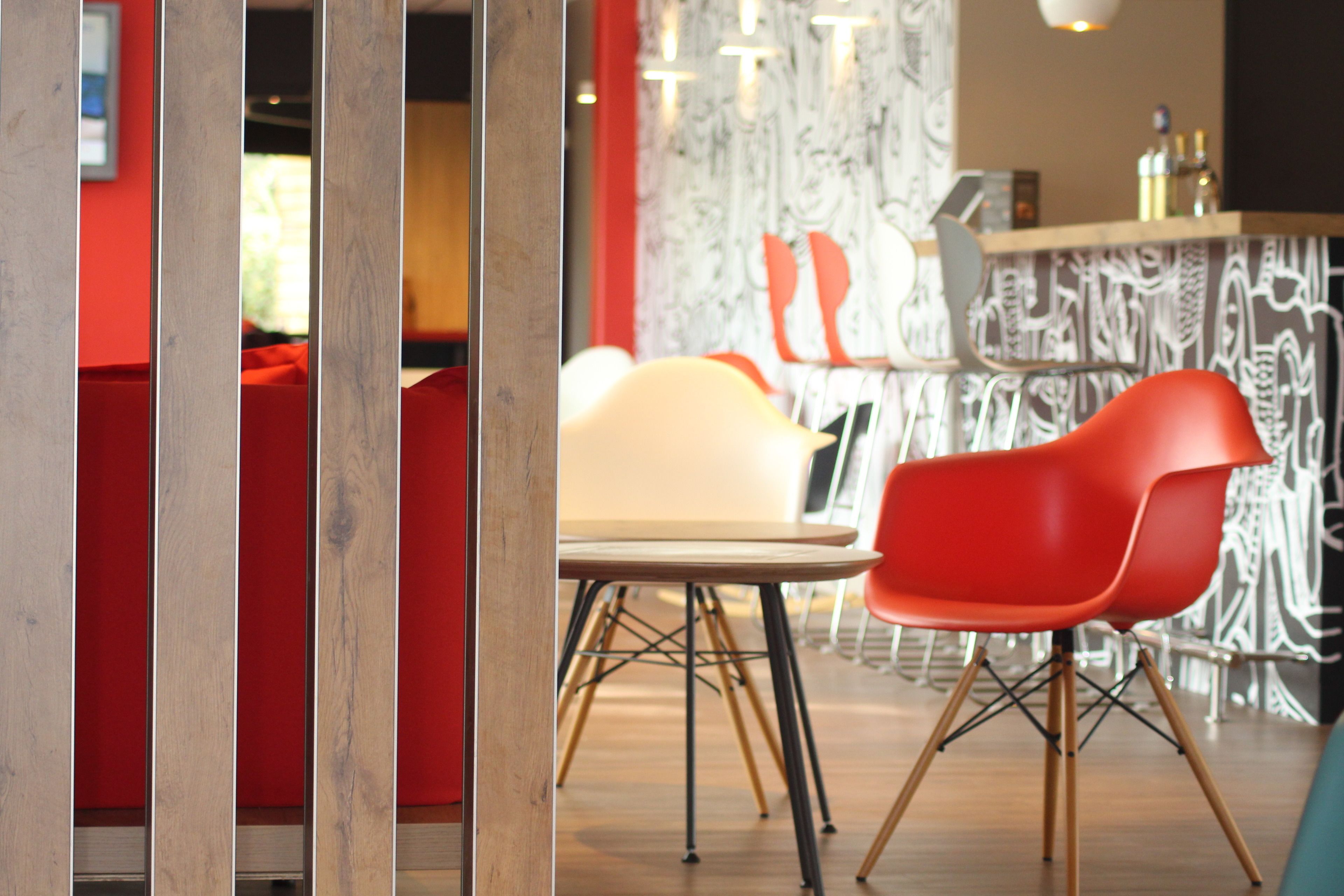 A modern interior with a wooden partition, a red and white chair, and a bar area with patterned wallpaper.