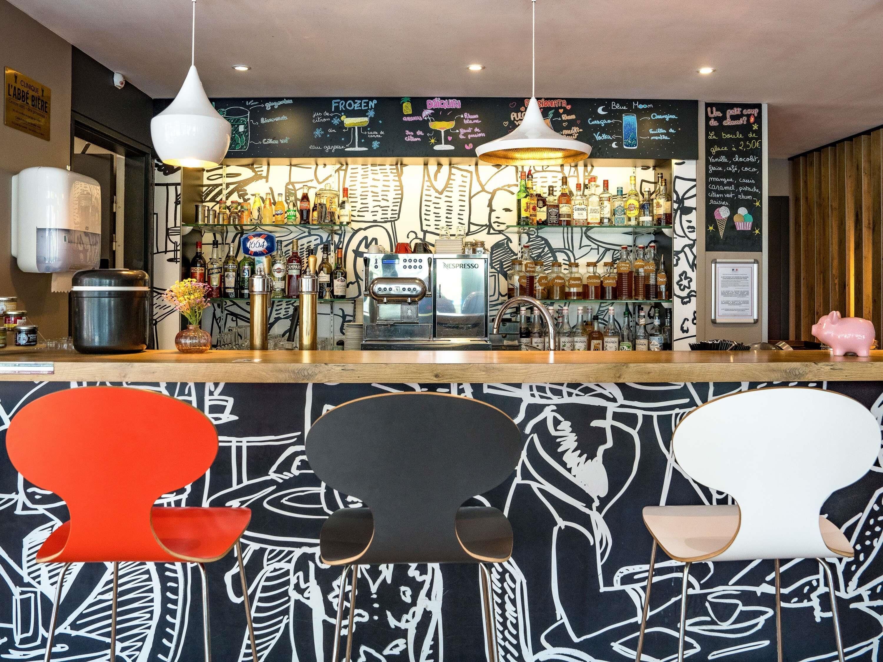 Zona de bar con menú en pizarra, diversas botellas, máquina de espresso y taburetes de estilo moderno.