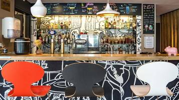 Zona de bar con menú en pizarra, diversas botellas, máquina de espresso y taburetes de estilo moderno.