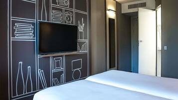 Une chambre d’hôtel avec un lit, un téléviseur à écran plat fixé au mur et une porte donnant sur une autre pièce.