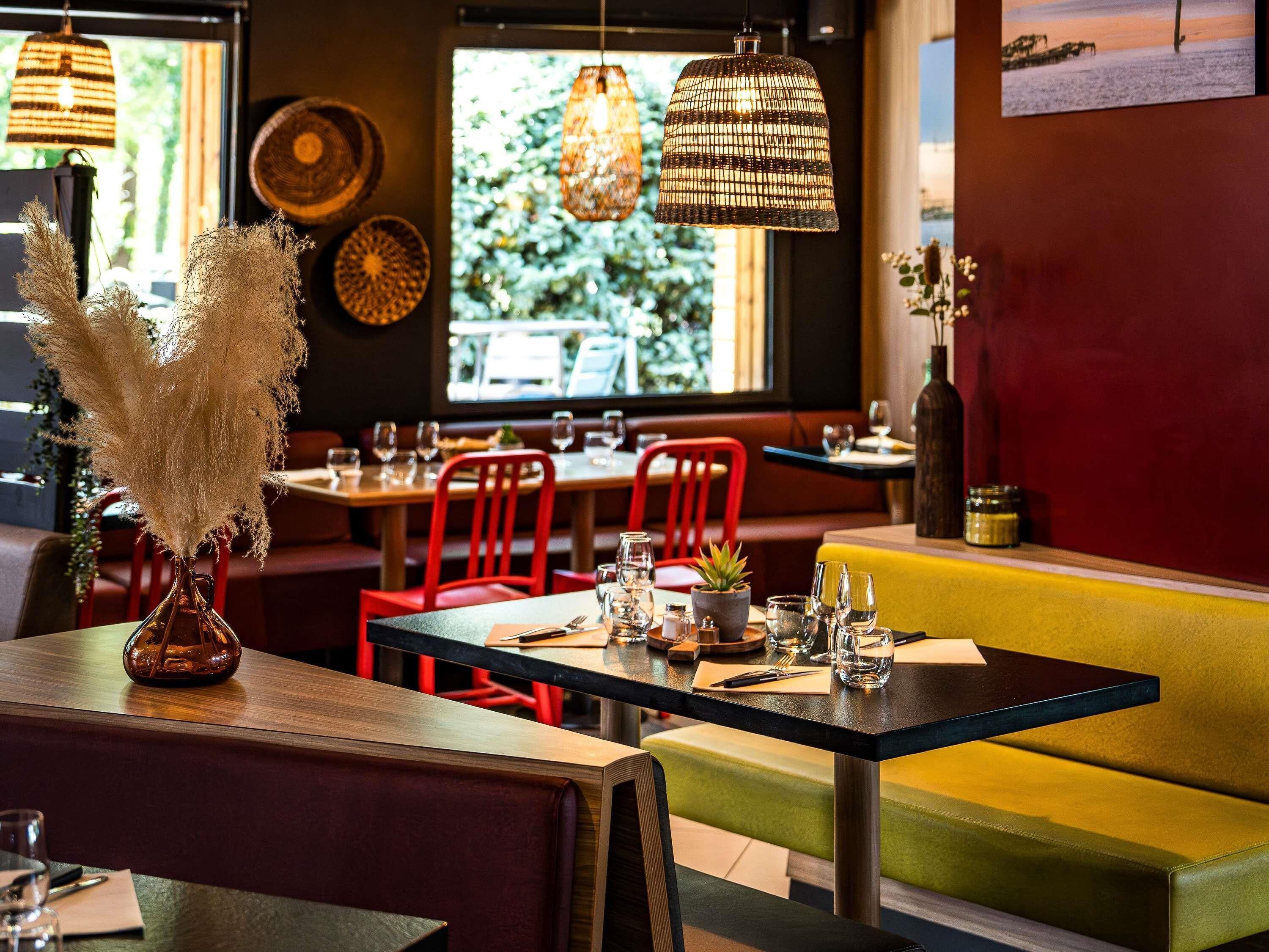 A restaurant interior with wooden tables, red chairs, a yellow booth, and hanging wicker lamps.