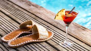 Eine Holzterrasse mit einem Paar gewebter Sandalen und einem Cocktailglas mit Ananas-Garnitur.