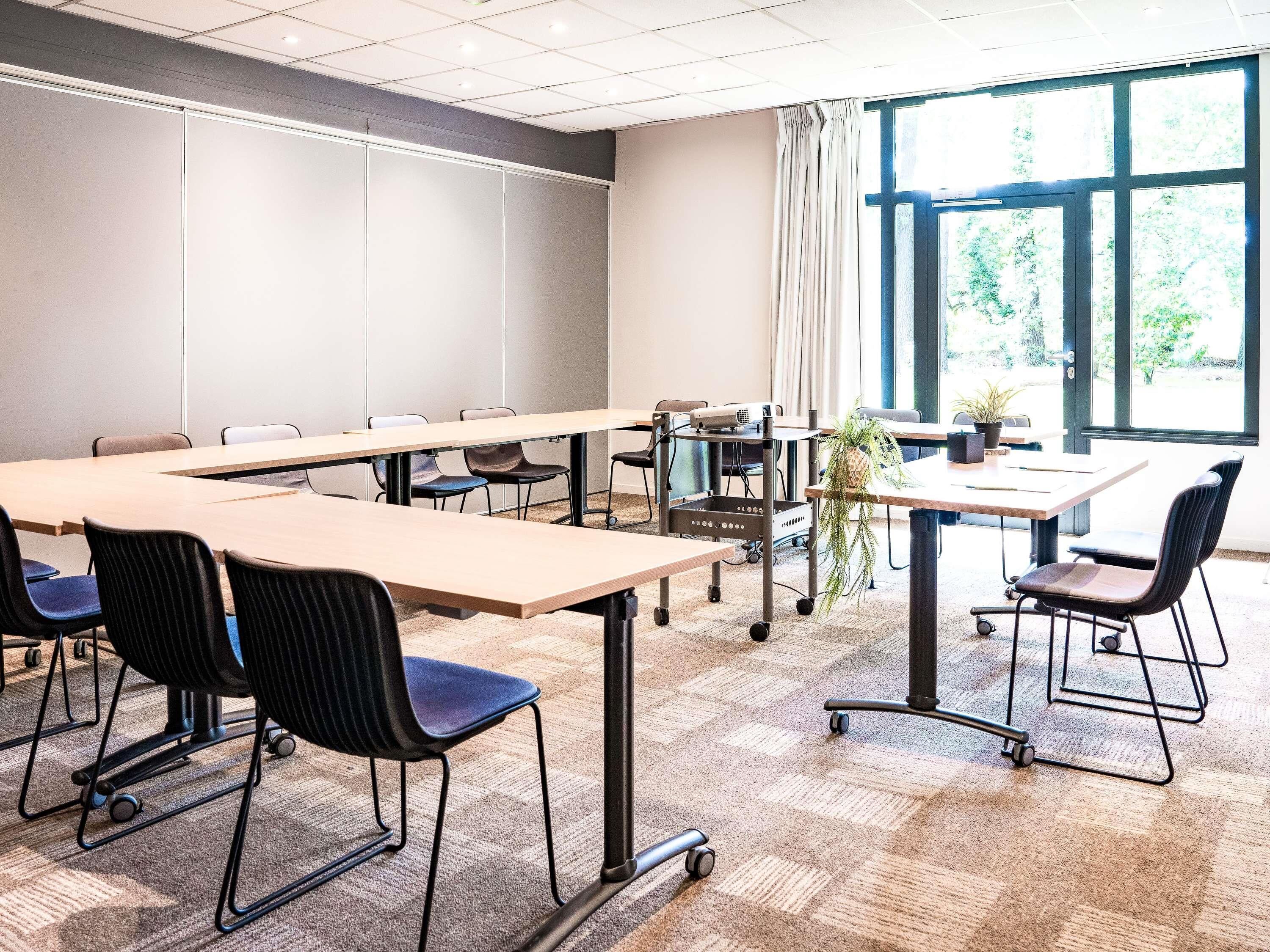 A conference room with a long table, chairs, a projector, and a plant.