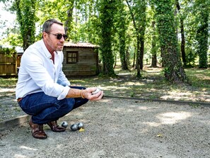 A man crouching on a gravel path with a ball and chain in a wooded area. - ibis Arcachon La Teste (La Teste-de-Buch)