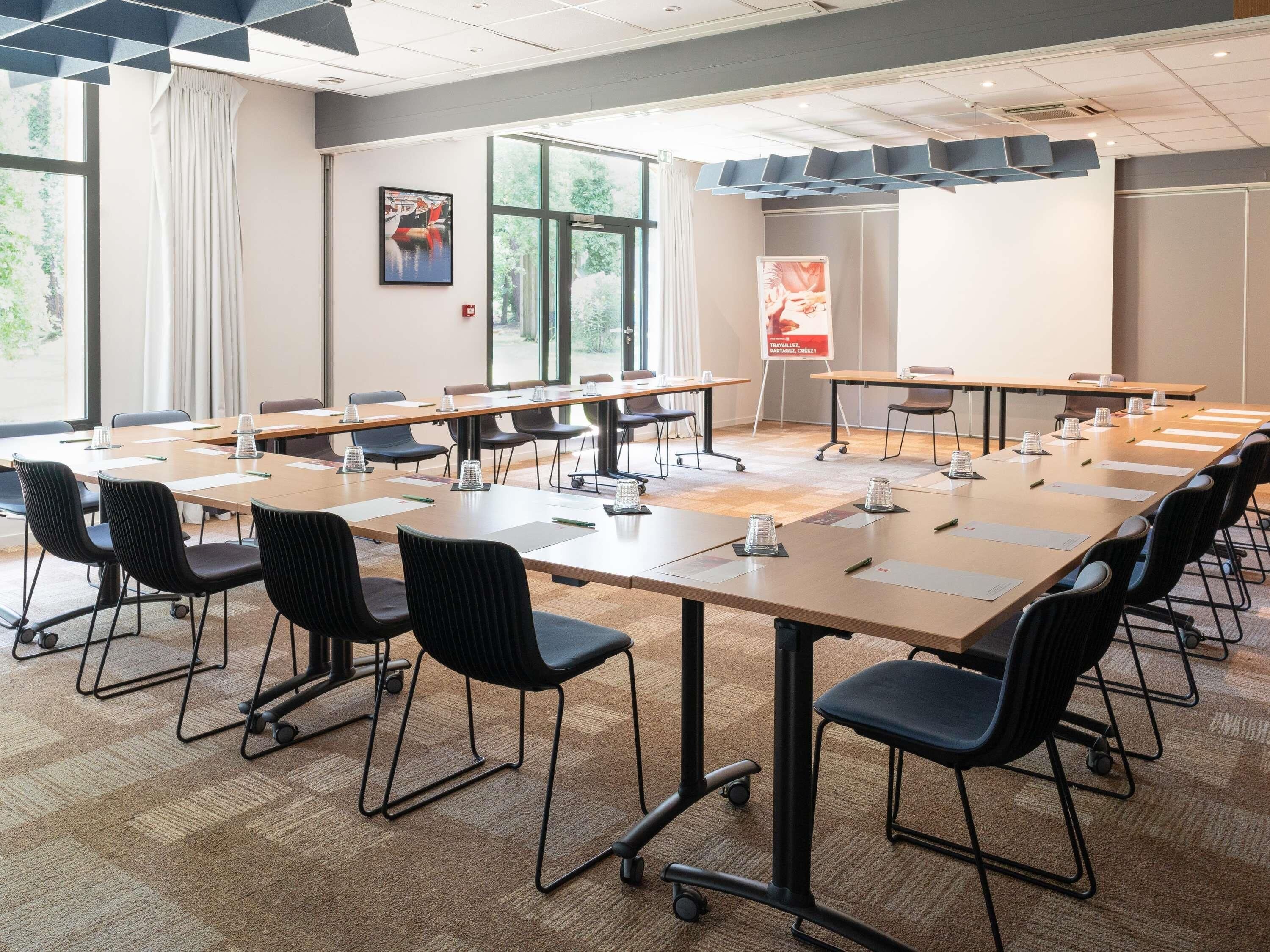 A conference room with multiple tables and chairs, large windows, and a poster on the wall.