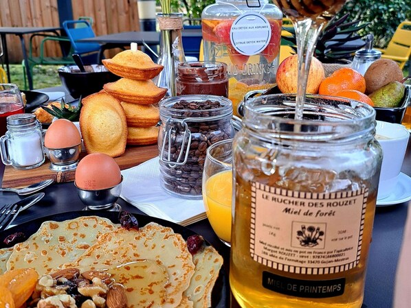 Une table de petit-déjeuner avec divers aliments, notamment des crêpes, des œufs et une bouteille de miel.
