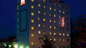 Un edificio de hotel de varios pisos con señalización iluminada que dice 'ibis HOTEL' y 'ibis HOTEL' en la fachada.