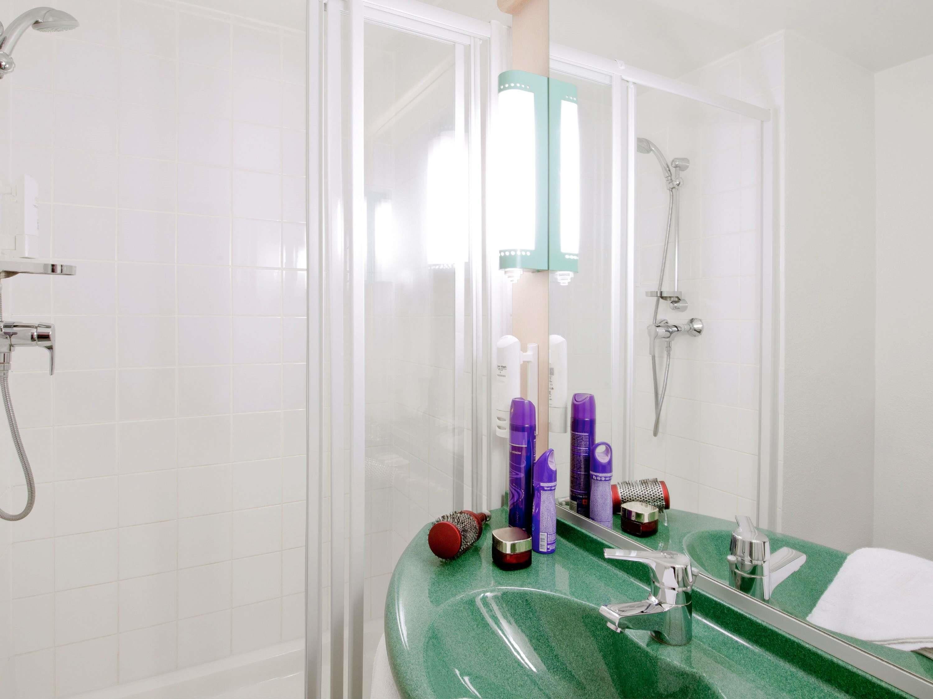 Une salle de bain avec un plan de toilette vert, un lavabo blanc, un miroir et un espace douche.
