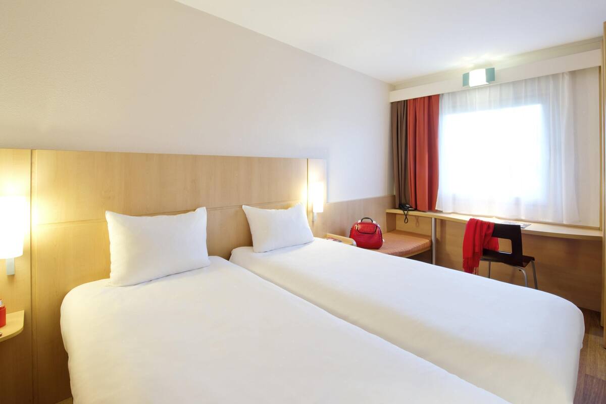 Habitación de hotel con cama doble, mesitas de noche, escritorio, silla y ventana con cortinas.